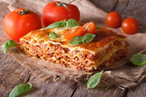 Italian lasagna with basil close-up on paper, horizontal rustic